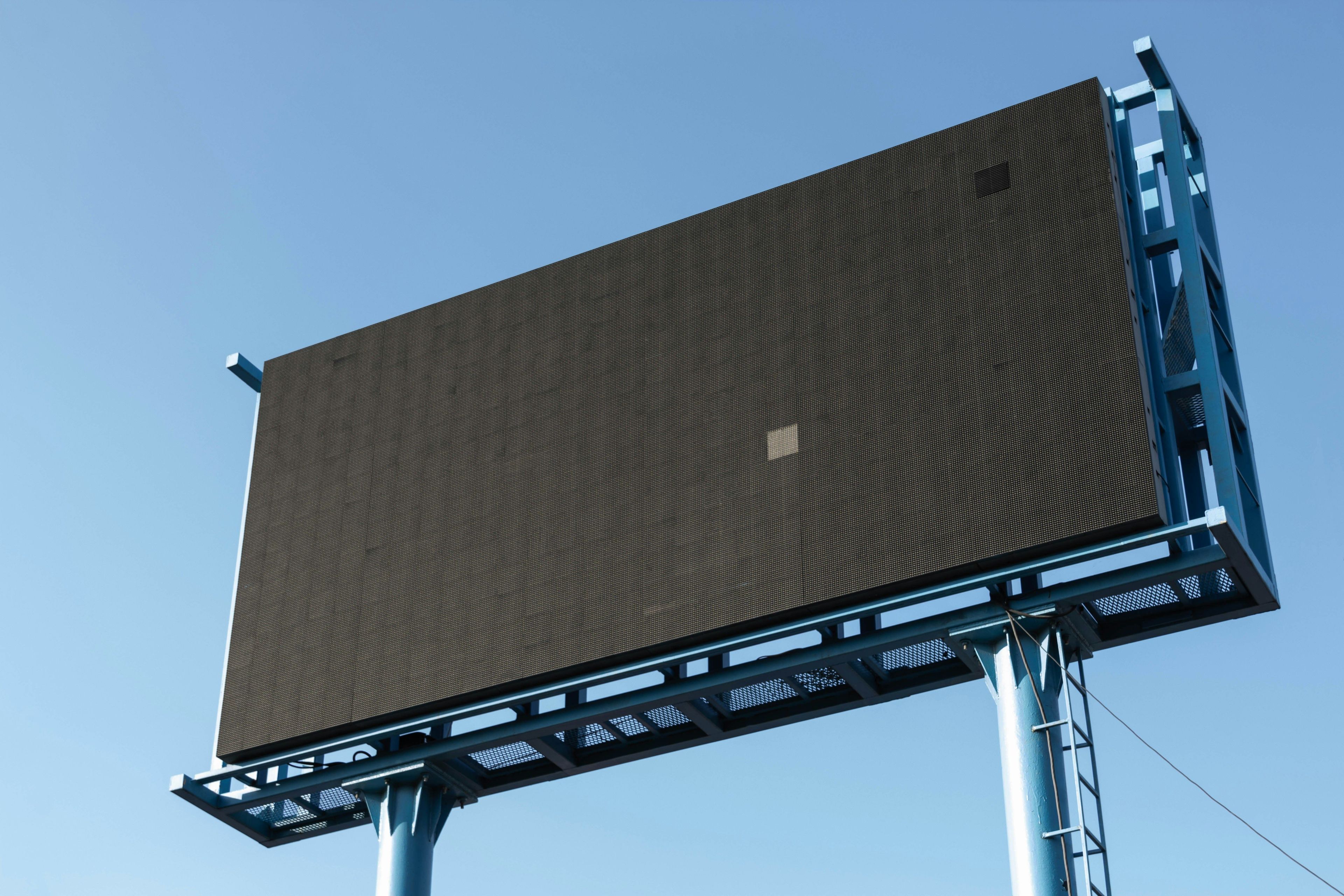 Große, leere schwarze LED-Werbetafel mit blauer Stahlkonstruktion vor klarem, hellblauem Himmel.